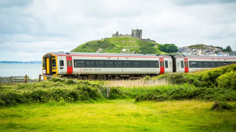 A train travelling alongside the coast and a castle on a hill.